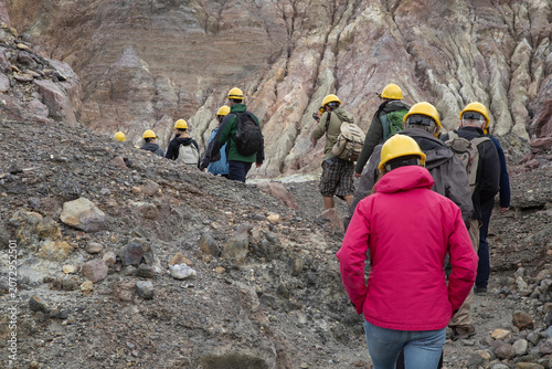 Group of tourists with guide at volcanic White Island, rough, barren landscape with rocks and lava in the crater