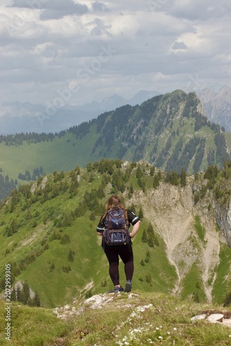 Cuadro en lienzo Back view of a girl with a backpack standing on a mountain peak and admiring the panoramic view of the alpine range on a summer day