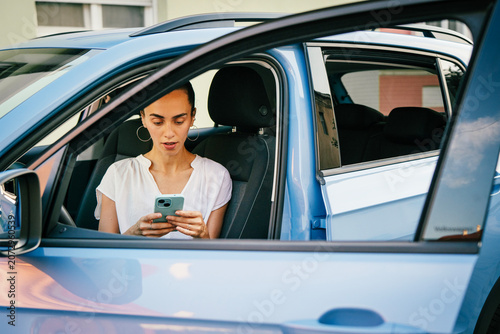 Young hispanic woman sitting in a car driver seat and using a smartphone application for parking payment or city map navigation