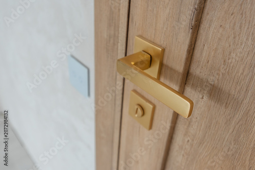 Closeup photo of modern wooden door with golden handle Close up of modern golden door handle on wooden interior door symbolizing completion of renovation and final finishing details