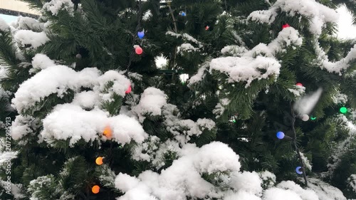 Christmas tree branches with a garland against falling snow.