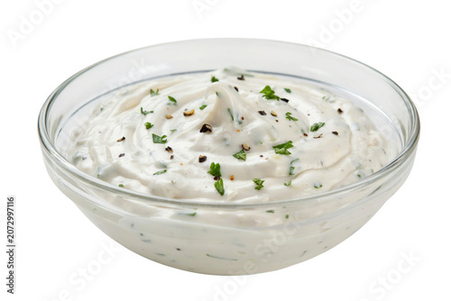 A small glass bowl filled with creamy white ranch dressing topped with fresh green herbs and cracked black pepper, isolated on white background