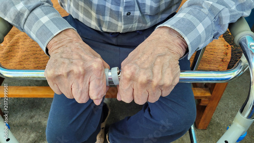 Vászonkép The wrinkled hands of an old man grip the handrails of a medical walker