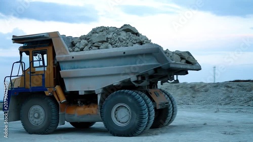 Huge mining dump truck moving stones in an open-pit quarry against a blue sky background