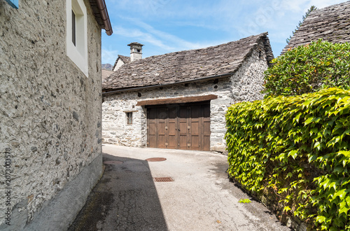 Traditional stone farmhouse with a characteristic gneiss stone roof located along a narrow street in the historic center of Maggia, Canton of Ticino, Switzerland.
