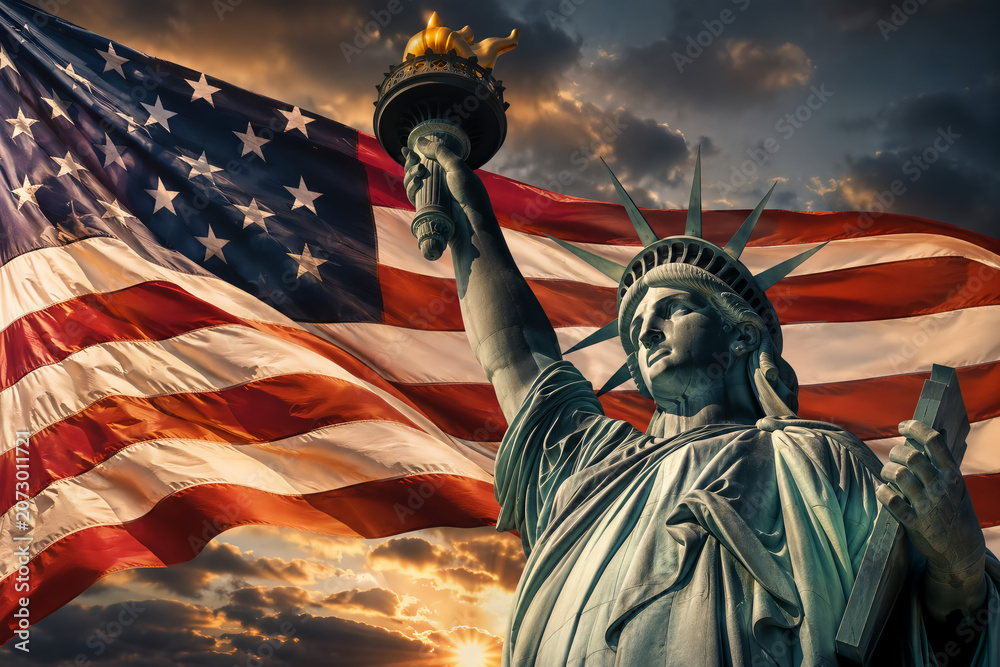 Obraz premium Statue of liberty against a large american flag at sunset