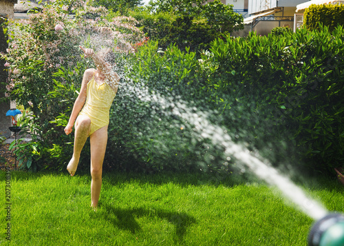 A cheerful child plays with water sprinklers in the garden during the summer. Creatively watering the garden—with fun and high spirits. An authentic, real little girl.