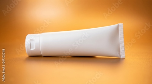 A white cosmetic tube lies on an orange surface with a subtle shadow.