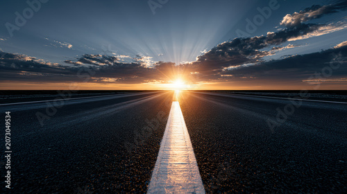Sunrise or sunset over an empty road with a white center line, dramatic clouds, and sun rays illuminating the horizon.