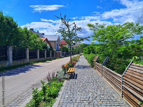 A cobblestone cycling path on Na Strance street along the EuroVelo 4 route, separated from railway tracks by a wooden barrier in Revnice.