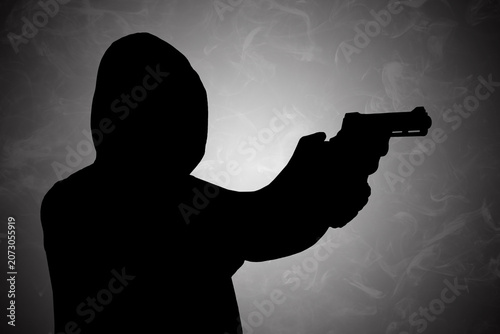 Mysterious dark silhouette of a hooded figure holding a handgun, presented against a moody, smoky background
