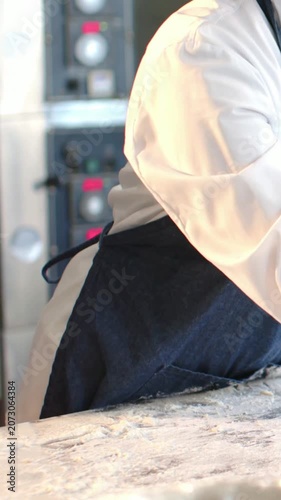 Vertical video: Leaning white-coated chef in jean apron stretching dough for baking, copy space