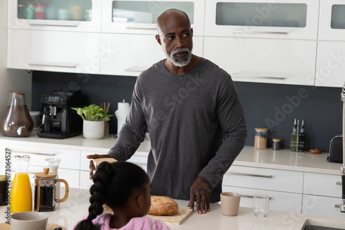 Senior African American man and daughter standing at kitchen island making toast with bread, coffee