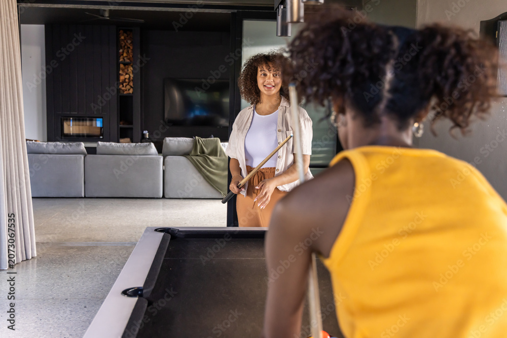 Naklejka premium Diverse female friends playing on pool table in game room, one wearing mustard top, holding cues