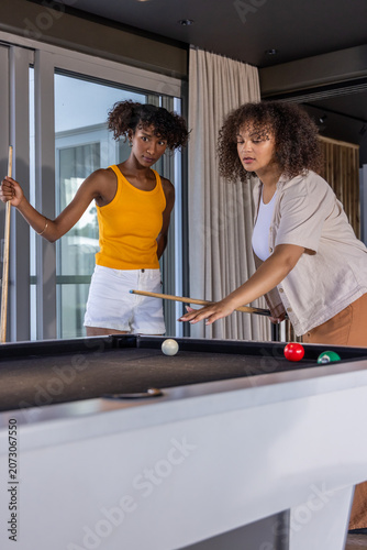 Diverse females playing pool at table with wooden cues in rec room, one lining up shot
