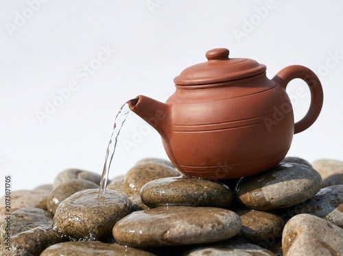 Terracotta teapot pouring water on wet stones