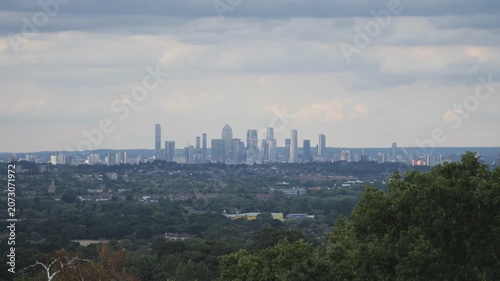 A distant London city skyline viewed over a lush green forest canopy.