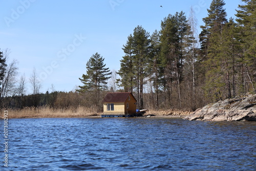 A small house standing on the water. Northern landscape. National park. Bay of water and forest on the crag. Spring. Republic of Karelia - Russia. Lahdenpohja. 
