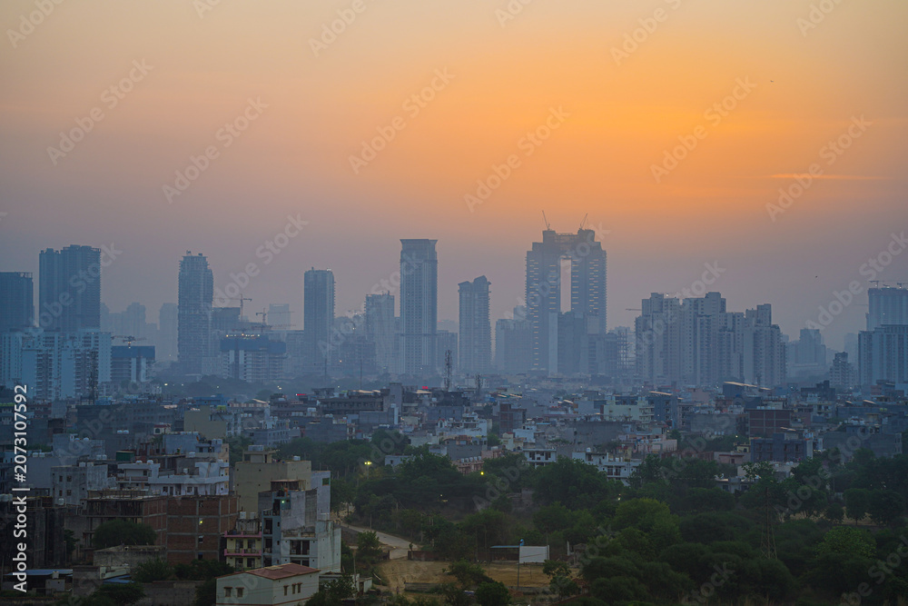 Fototapeta premium Aerial drone panning shot sunrise high rise skyscraper buildings at hidden in smog showing the cityscape of Gurgaon Delhi India
