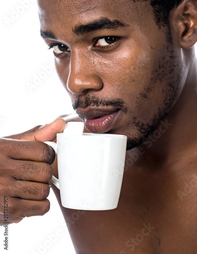 A close-up of a shirtless man drinking from a white mug