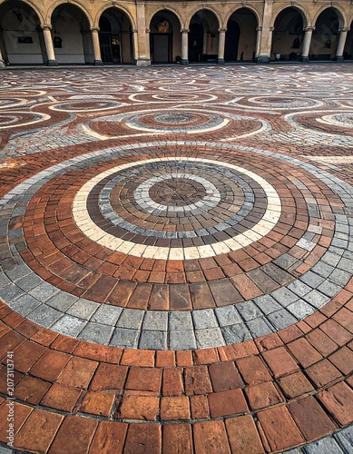 A circular mosaic pattern on a brick floor with arched walkways