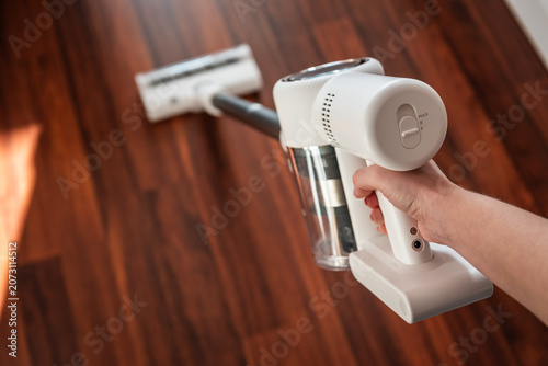 Fotografía Woman using a powerful white cordless vacuum cleaner on a dark hardwood floor, ergonomic design for effortless home hygiene and spotless surface