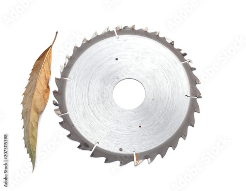 A circular saw blade with a dry leaf beside it on a white background