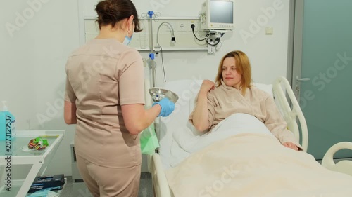Nurse carries metal tray after arm care near hospital bed. Woman bends arm with cotton pad watching medical worker finish procedure