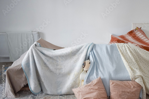 Foto A homemade blanket fort built in a white bedroom using pillows, bedsheets, and chairs