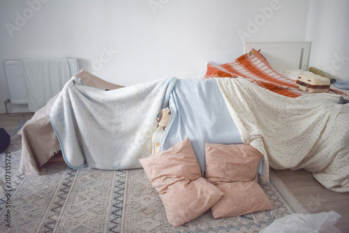 Cuadro en lienzo A homemade blanket fort built in a white bedroom using pillows, bedsheets, and chairs