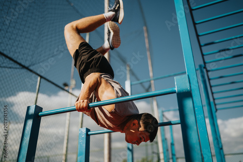 Fotografie A fit man holds an inverted calisthenics pose on parallel bars