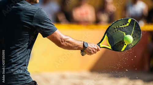 Beach tennis player mid action striking the ball during a sunny outdoor game