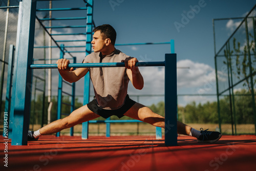 Photos Young man performs a wide straddle stretch while holding onto outdoor calisthenics bars
