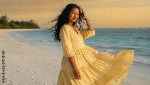 Young Asian Woman in Flowing Yellow Dress Standing on Tropical Beach with Windblown Hair at Golden