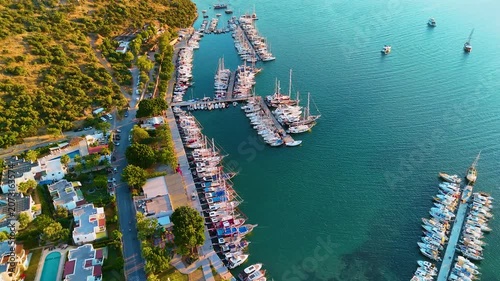 Cinematic aerial drone slow forward shot over Bitez Marina with sailing yachts, Turkish gulet boats and luxury motorboats at golden hour sunset, Bodrum Aegean coast Mugla Turkey