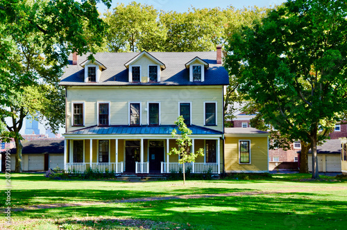 Foto Historic yellow clapboard outbuildings and large tree on Governors Island park g