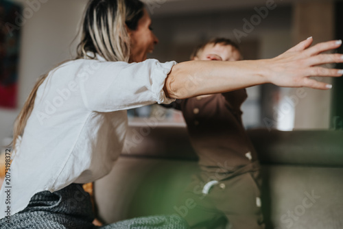 Fotografie A mother reaches out to embrace her toddler on a living room couch