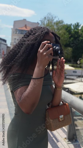 Young black woman traveler taking a photo with a camera on the street on a sunny day in Europe, Nis, Serbia