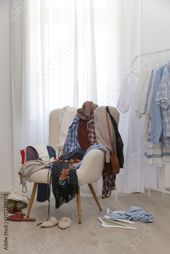 Obraz na plátne Armchair covered with clothes, used as a clothing drop zone, representing everyd