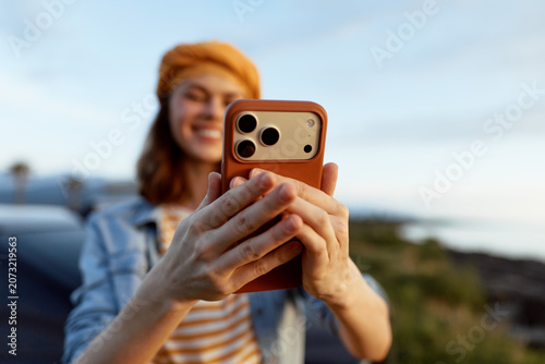 Konstfotografi Young woman wearing a striped shirt and orange hat takes a sunny outdoor selfie, smiling into the camera while the breeze rustles her hair