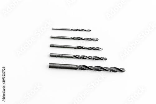 Set of metal twist drill bits in different sizes arranged by diameter on a white background. Drilling accessories for woodworking, metalworking, construction and DIY projects.