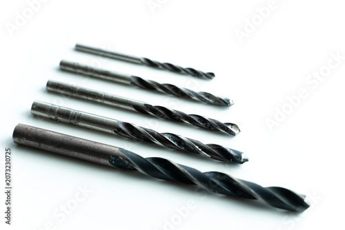 Five metal twist drill bits of different sizes isolated on a white background. Professional drilling accessories for woodworking, metalworking, construction and industrial applications.