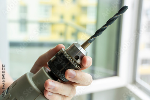 Close-up of a person holding an electric drill with a metal drill bit installed in the chuck. Power tool ready for drilling, repair, construction and home improvement.