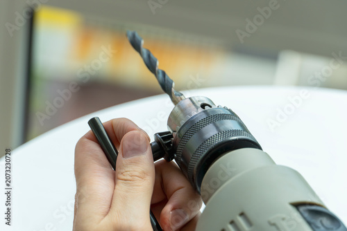 Close-up of a person tightening the drill chuck with a chuck key on an electric drill before drilling. Power tool preparation, DIY, construction and home renovation concept