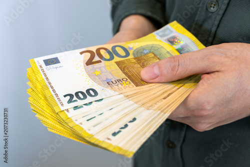 Close-up of hands holding a large stack of 200 euro banknotes. European currency, cash payment, savings, wealth and financial success concept.