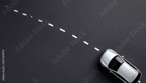 Top flat lay view photo of toy mini car driving on asphalt road with headlights direction on isolated background with copy empty space. 