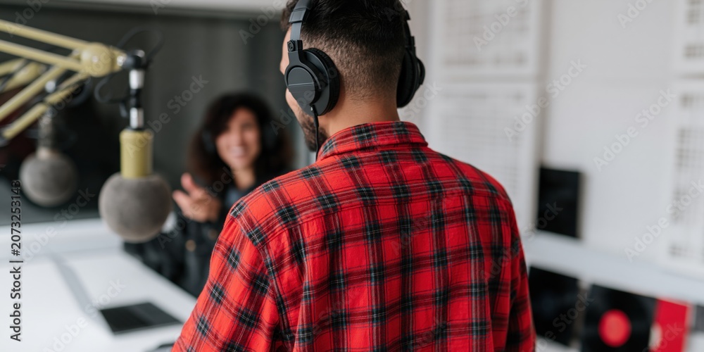 Naklejka premium Podcast host in a recording studio wearing headphones and a red plaid shirt for radio interview background and broadcast banner design