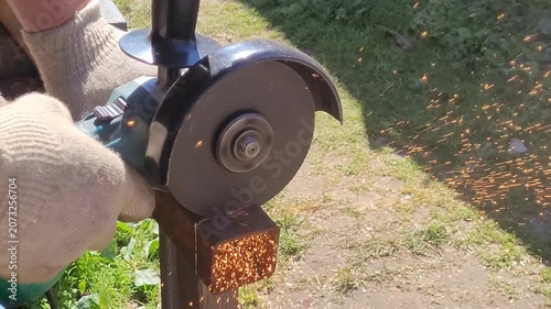 Male hand cuts off pieces of pipe with angle grinder. Cutting of a steel with splashes of sparks at construction site. Sparks during cutting of metal angle grinder