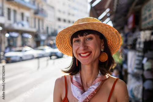 A stylish young woman in a hat and fashionable clothing poses while standing in the middle of the street.