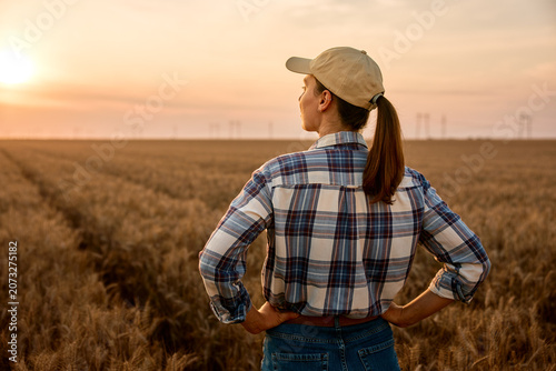 Fotografia Female farmer standing in wheat field at sunset looking forward